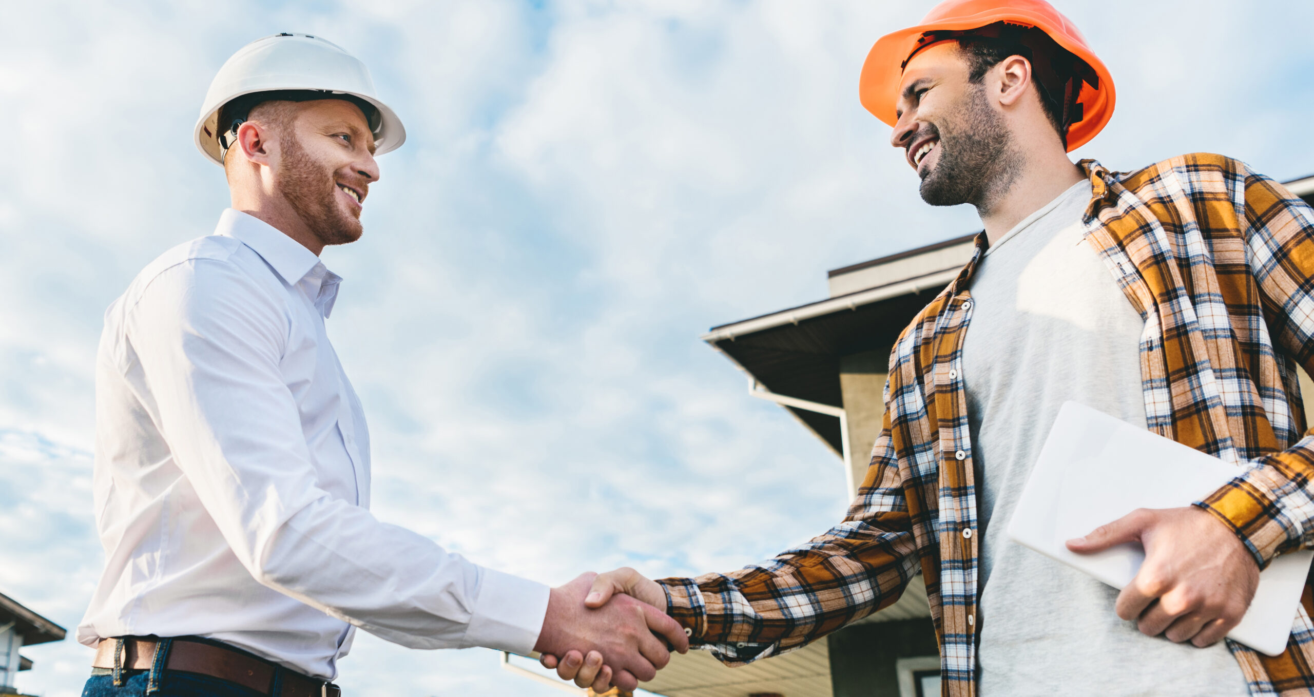 bottom view of smiling architects shaking hands in front of construction site